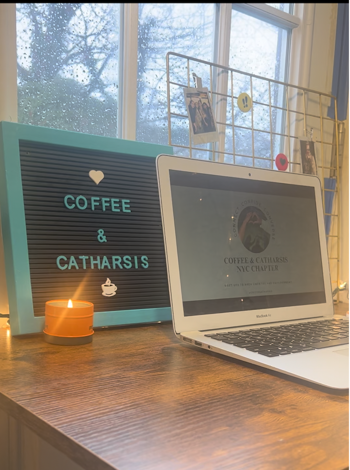 A laptop on a wooden desk showing a video call of several people in conversation, beside a mug of coffee.